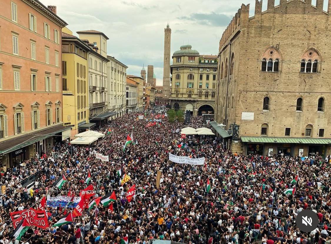 Crowds of people taking part in Italy Pro-Palestine Protests, marching through city streets with banners and flags.