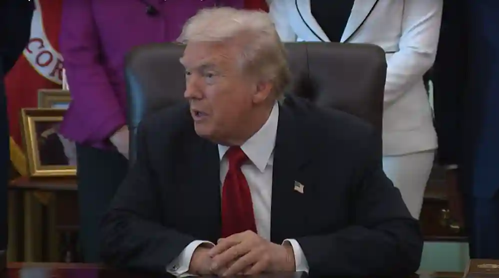 Donald Trump speaking at a press conference while gesturing, with a serious expression.