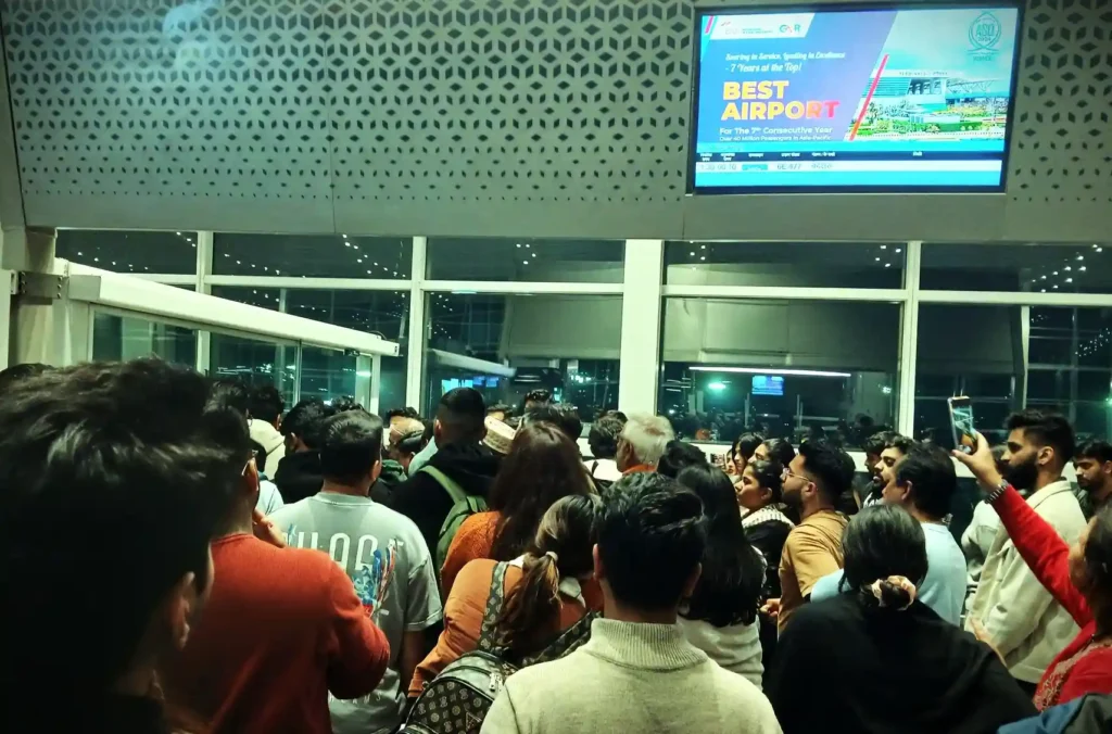 Passengers crowding outside an airport gate during IndiGo flight delays, waiting for updates amid confusion and mismanagement.