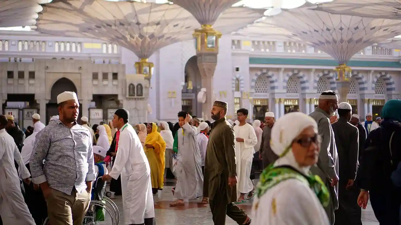 A diverse crowd of Muslim pilgrims walking through a large open courtyard with architectural canopies overhead, reflecting cultural and social context relevant to the Kuwait citizenship crackdown.