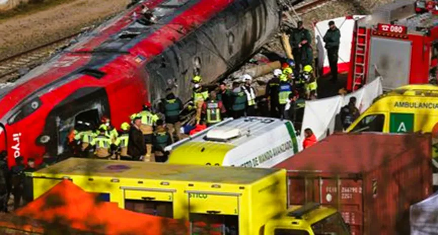 Emergency responders work at the crash site after the Adamuz train derailment in southern Spain, with derailed carriages and rescue vehicles visible.