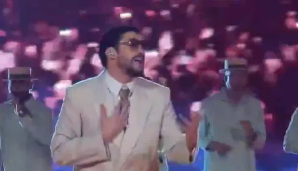 Bad Bunny performing during his Super Bowl halftime show in a beige suit on a brightly lit stage